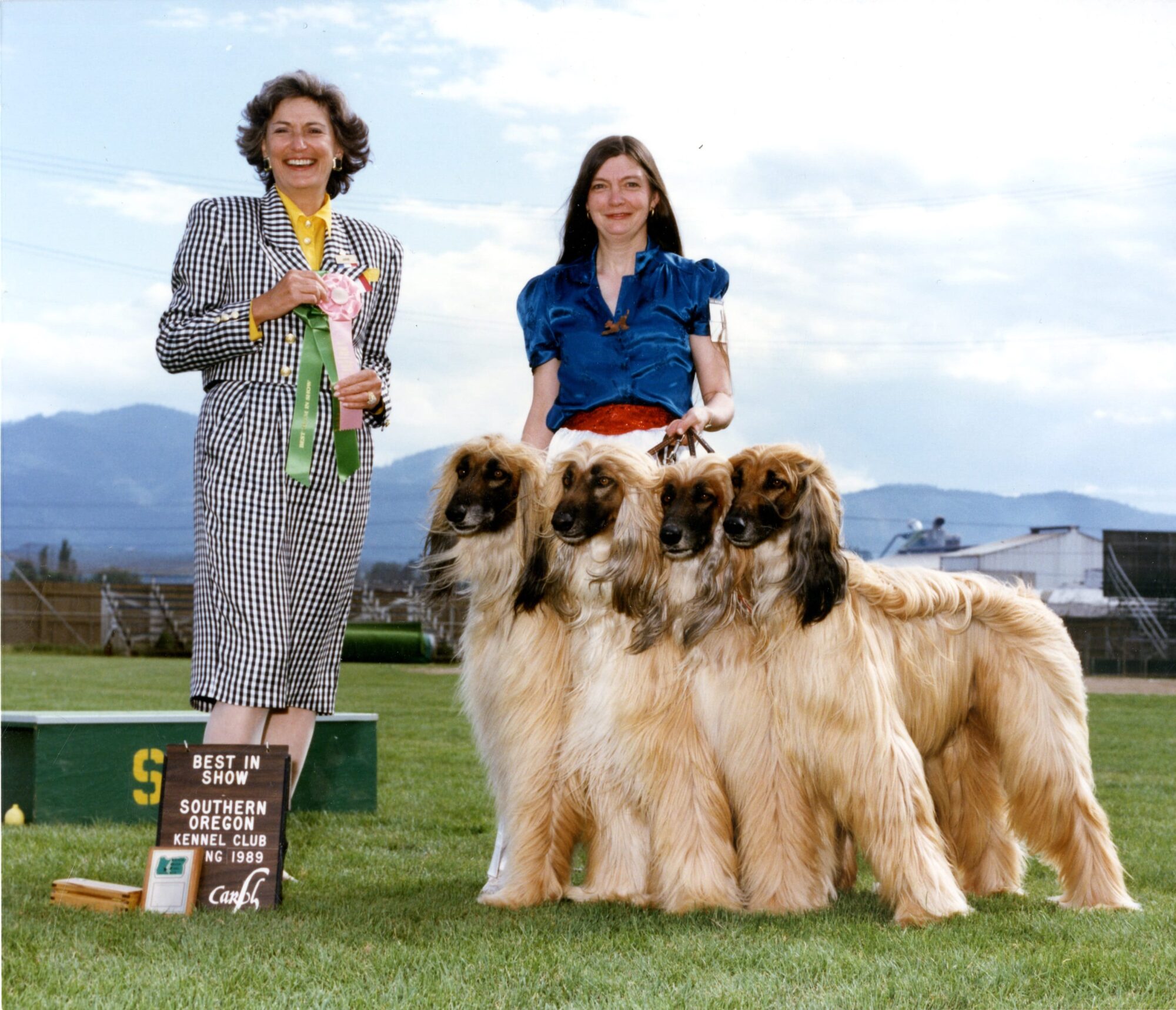 two women, one holding prize ribbons and the other holding four leashed Afghan Hounds. A sign reads "Best in Show, Southern Oregon Kennel Club, 1989.