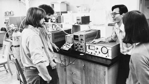 Four students in laboratory standing by electronic testing equipment