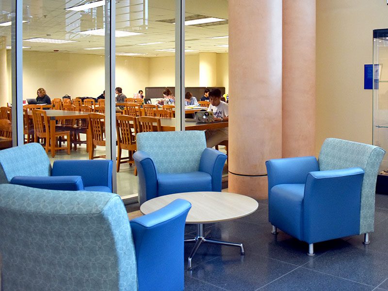 circle of upholstered chairs with students working at tables in the distance