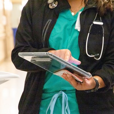 Medical resident at UC Davis Health wearing stethoscope and scrubs clicks on tablet