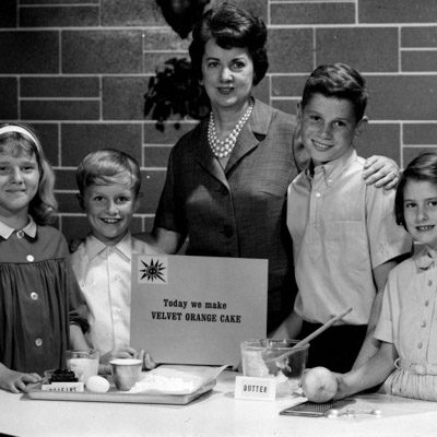 Black and white image of Ruth Ellen Church surrounded by children behind a table with cooking ingredients