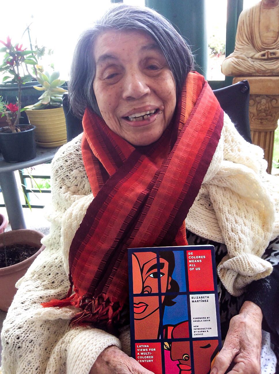 Betita Martinez, holding a copy of her book De Colores Means All of Us