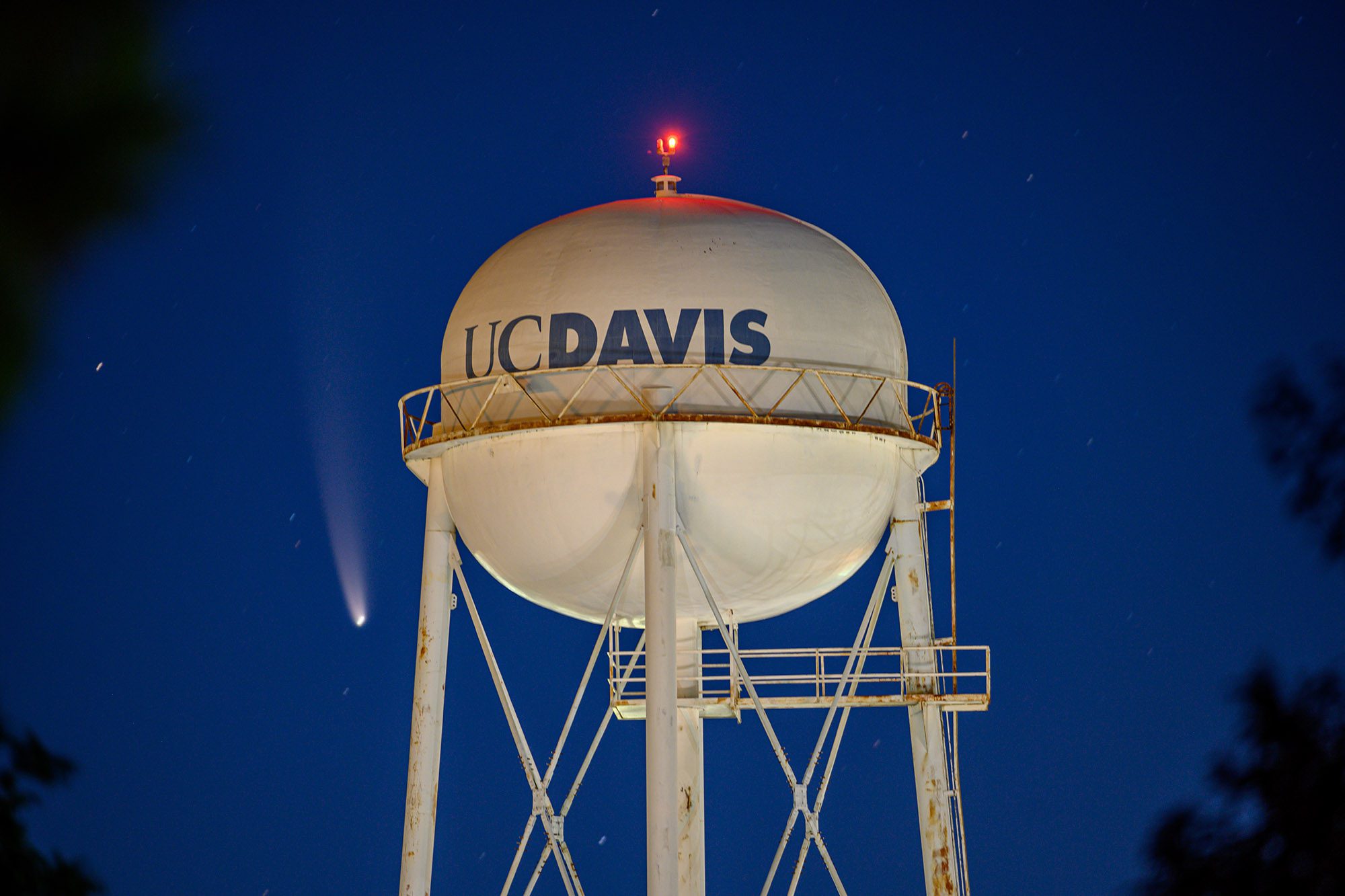 Water tower lit up at night with comet in the sky