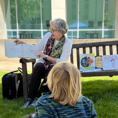 English Professor Fran Dolan seated and smiling, holding an open storybook while a small child looks on.