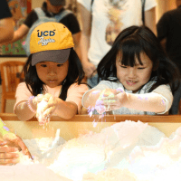 two girls with holding handfuls of sand above the AR Sandbox