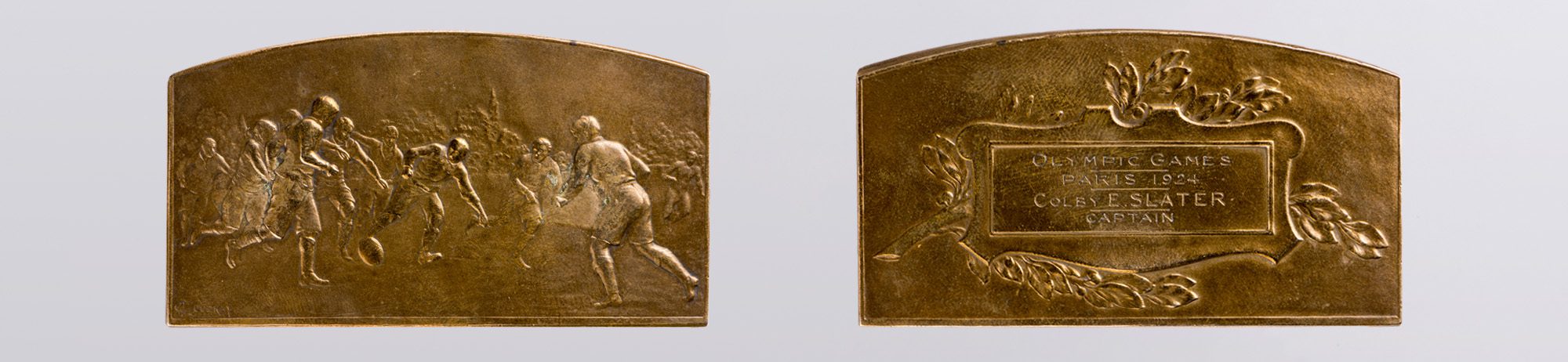 Two gold medals, side by side. The one on the left is imprinted with an illustration of a rugby match. The one on the right is engraved with the words "Olympic Games, Paris 1924, Colby E. Slater, Captain"
