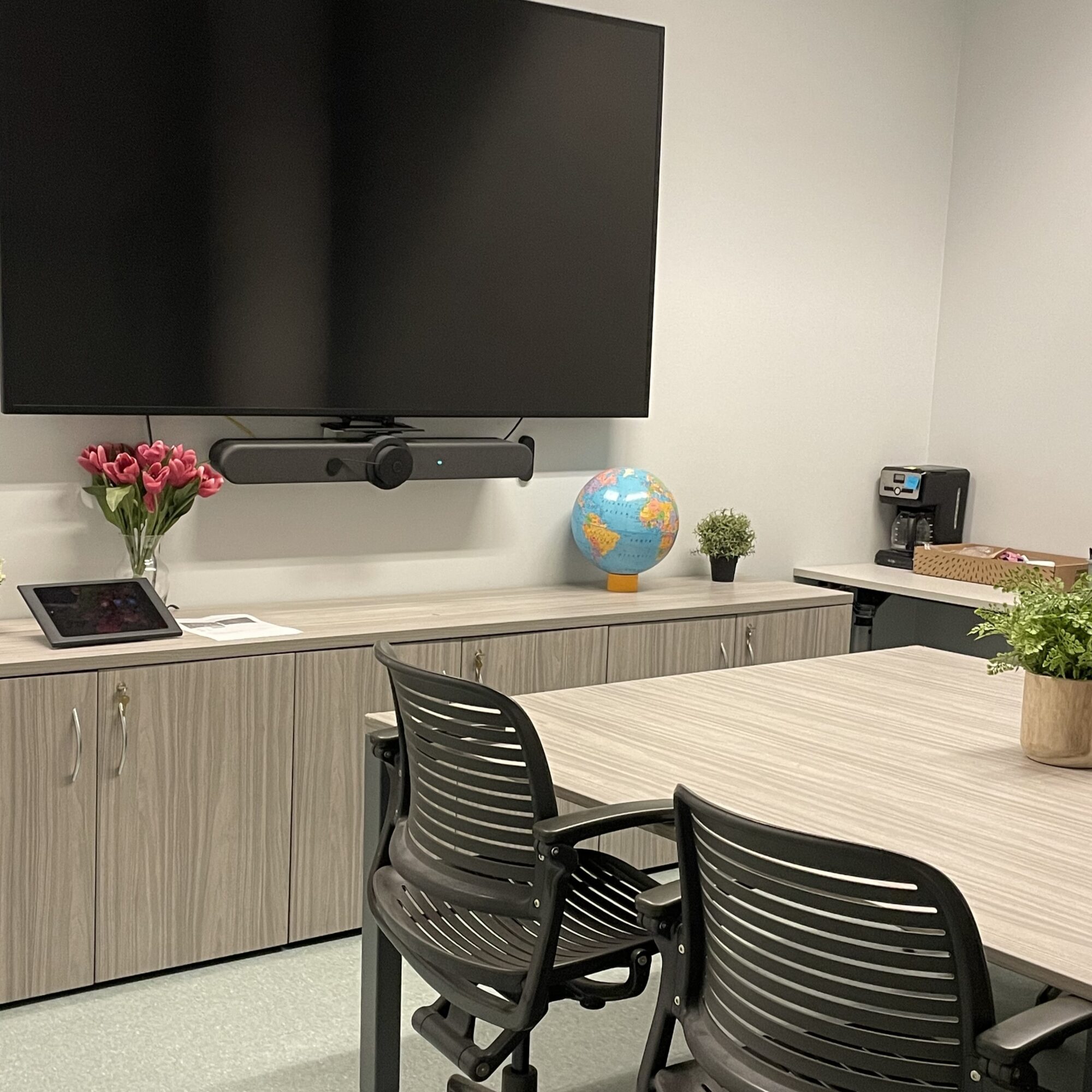 Employee break room with office chairs, flowers, coffee maker and large screen for Zoom meetings