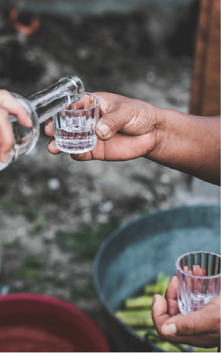 A hand from one person pours mezcal into the cup of another's.