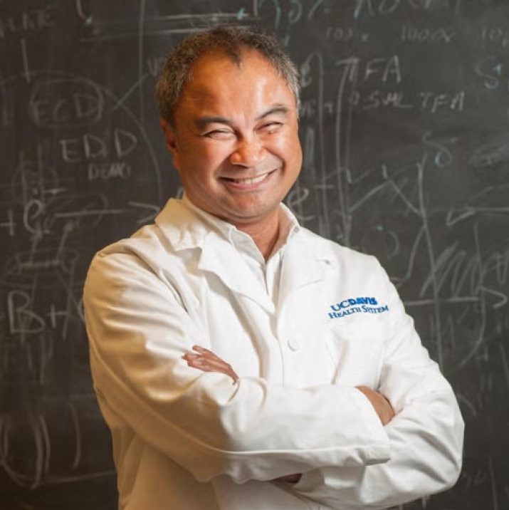 Dr. Carlito Lebrilla stands in front of a chalkboard, wearing a white lab coat with the UC Davis Health System logo embroidered on the front.