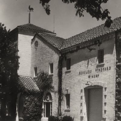 Black-and-white photo of a stone building with a tiled roof and sign that reads Beaulieu Vineyard Winery.