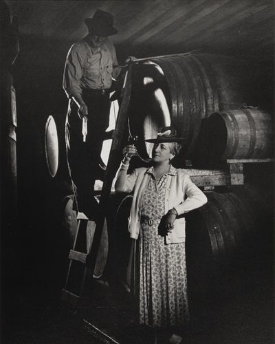 Fernande de Latour holds a glass of wine in front of wine barrels in a wine cellar