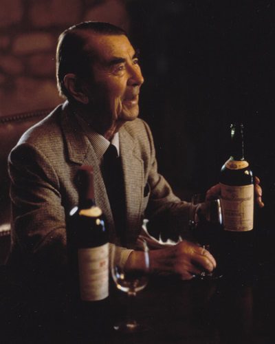 André Tchelistcheff holds a bottle of wine. Another bottle and a wine glass are in the foreground.