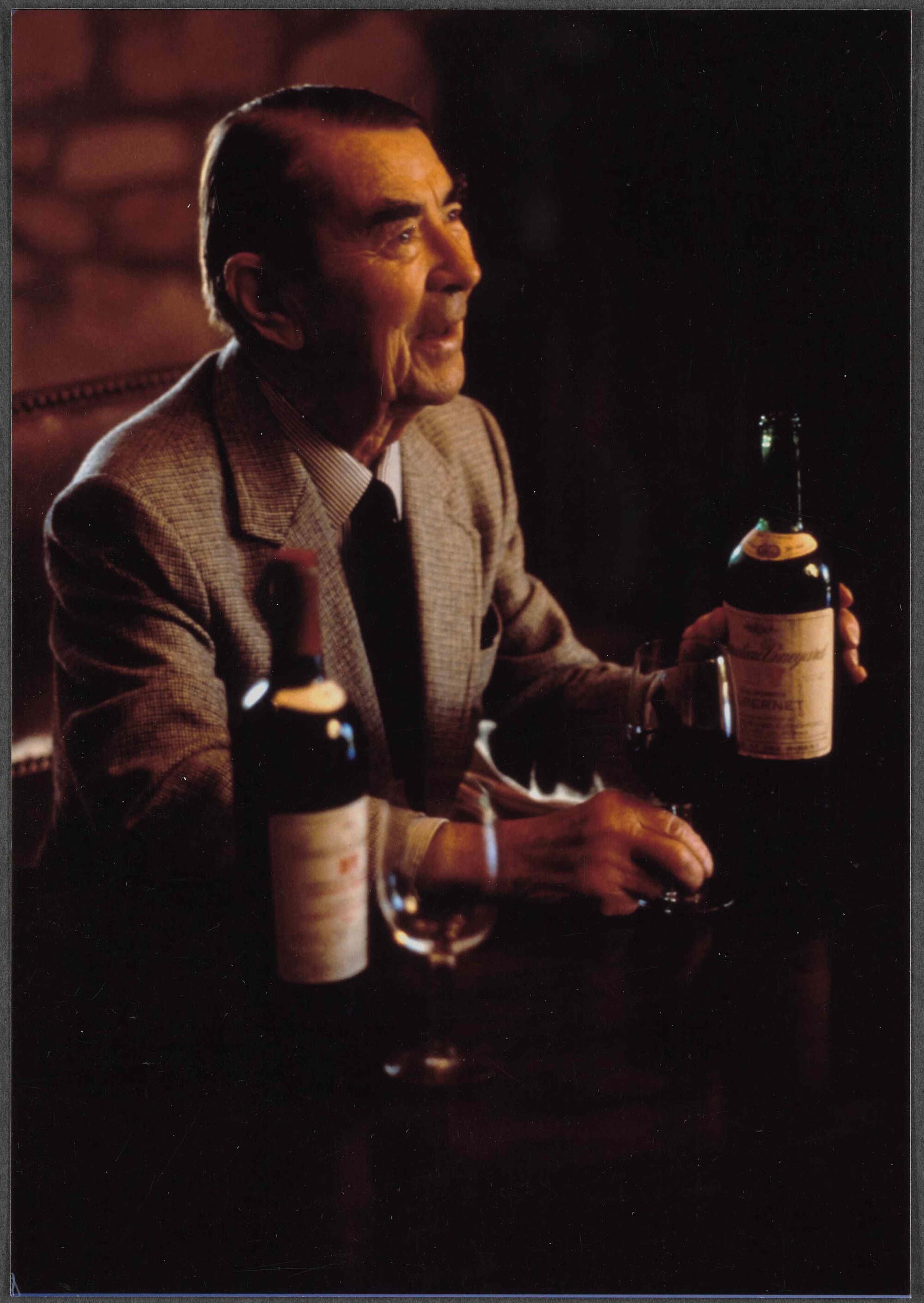 Andre Tchelistcheff, seated, holding a wine bottle, smiling