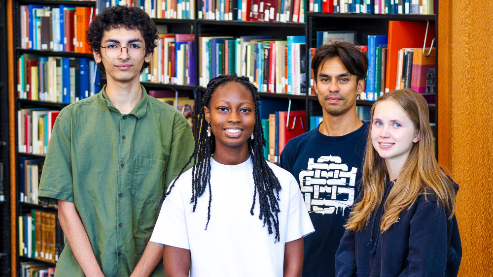 Four undergraduate interns standing in front of bookcases, smiling.