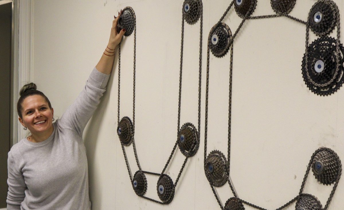 Bianca Iosif stands next two the letters UC made from bike chains and hubs, smiling.