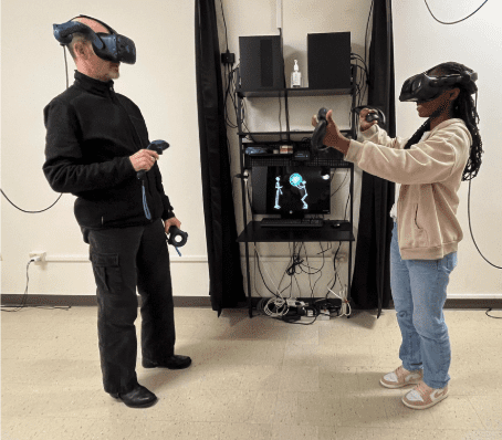 Two people facing one another wearing virtual reality headsets and holding controllers.