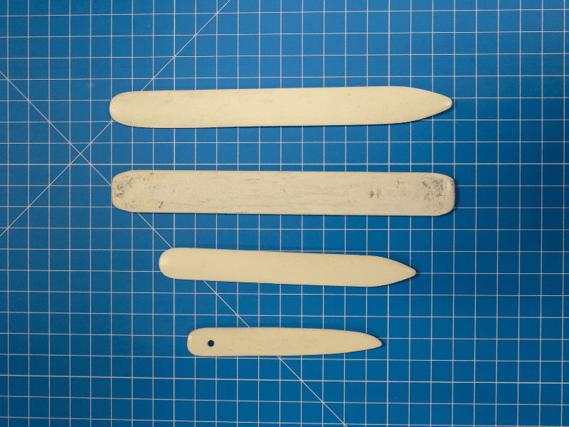 Four bone folders of various size, on a blue gridded mat.