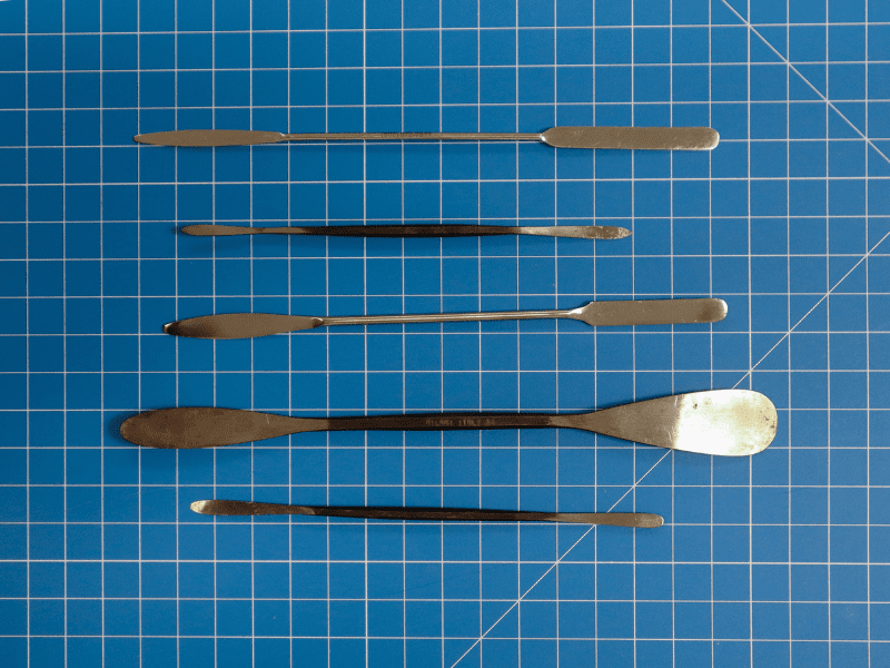 5 metal microspatulas of various size on a blue gridded mat.