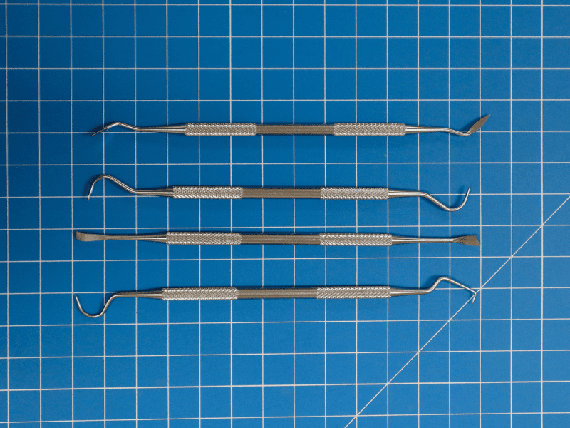 Four dental tools on a blue gridded mat.