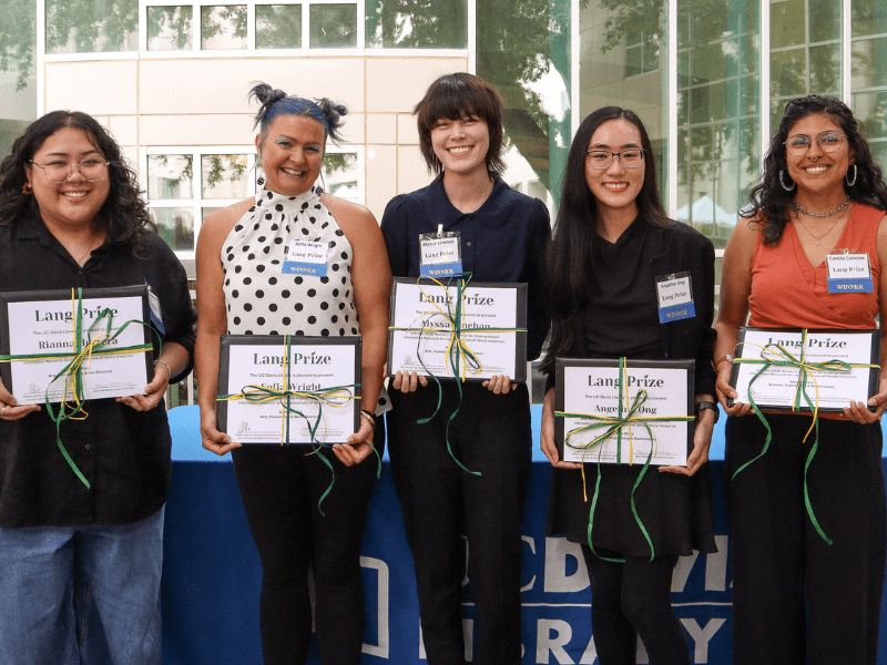 Five undergraduate students holding prize certificates, with the UC Davis Library logo just visible on the tablecloth behind them.