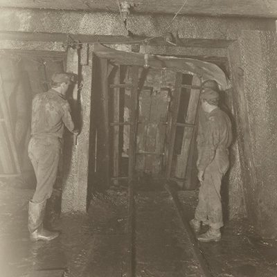 Interior of mine shaft, two miners have their backs to the camera