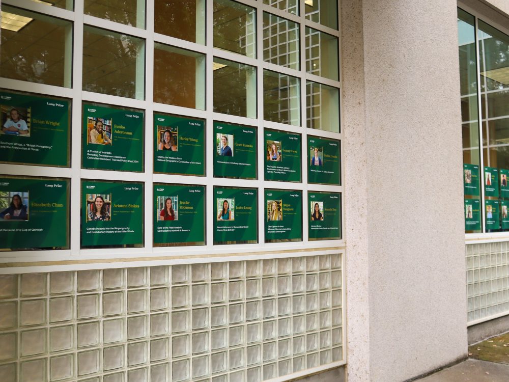 Two rows of posters with green backgrounds and photos of past prize winners line the Shields Library Courtyard windows.