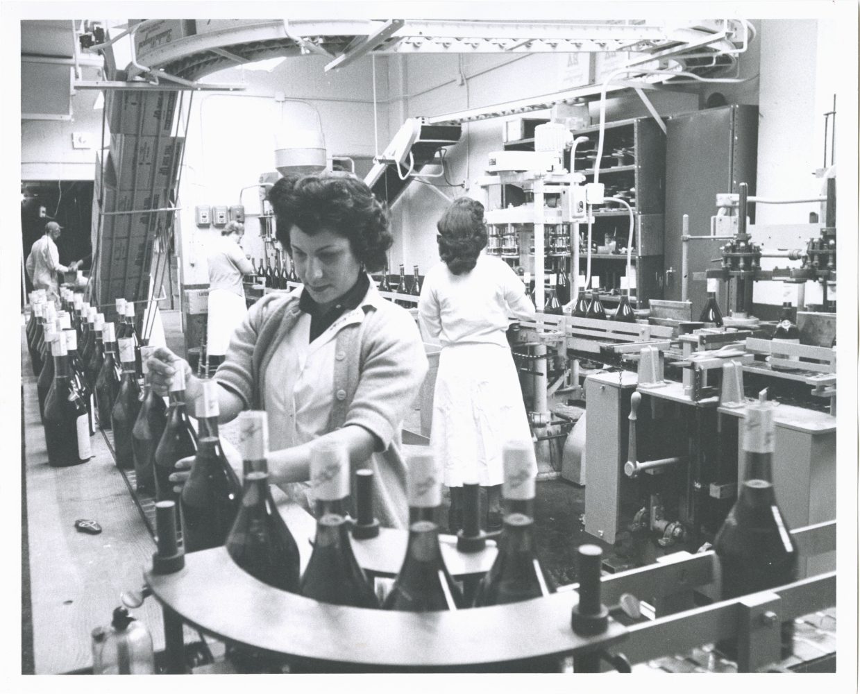 Two women inspect bottles on an assembly line.