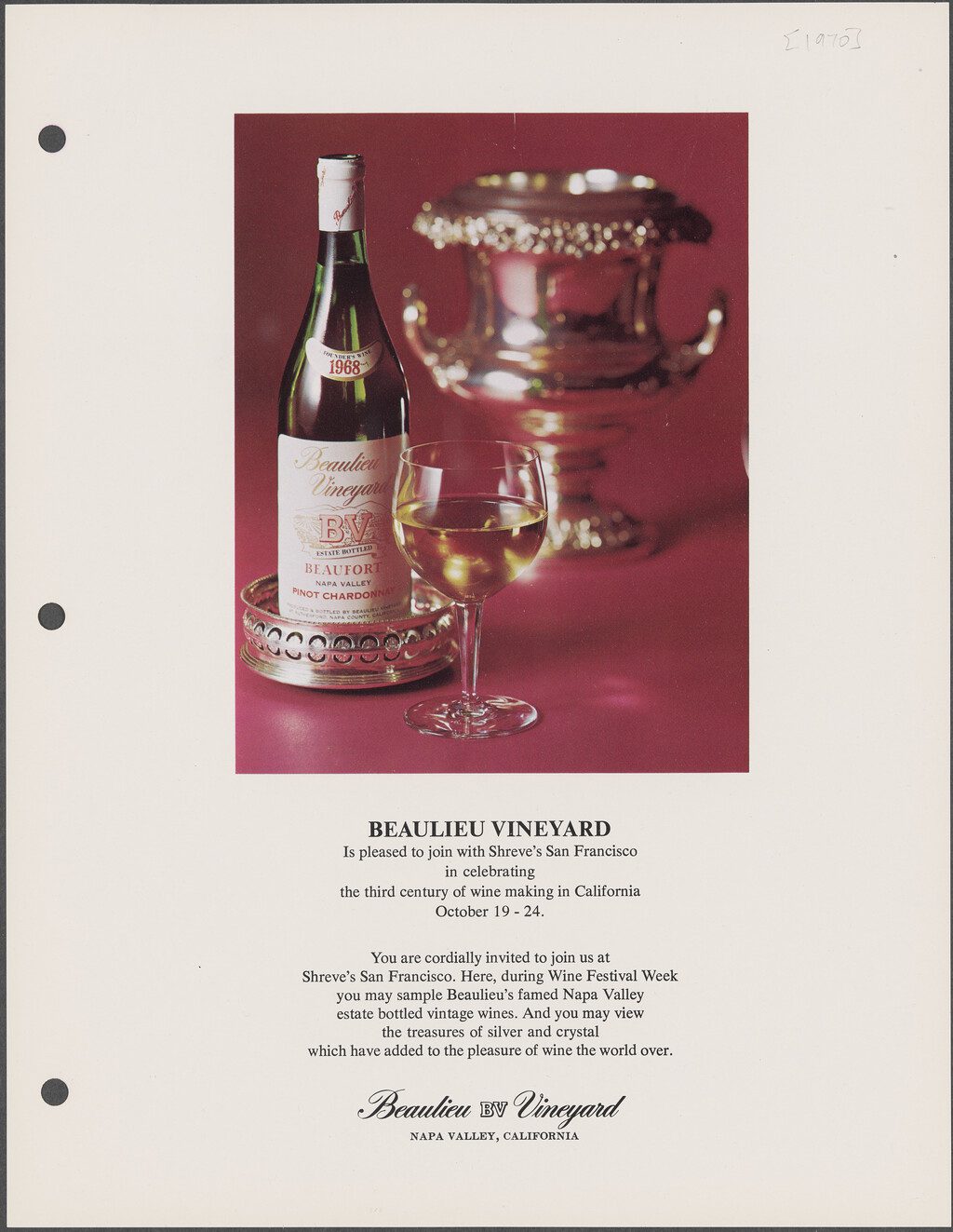 A bottle of 1968 Beaulieu Vineyard Beaufort Pinot Chardonnay sits on a sterling silver bottle coaster, alongside a glass of white wine and an ornate silver bottle holder, on a deep rose-pink background.