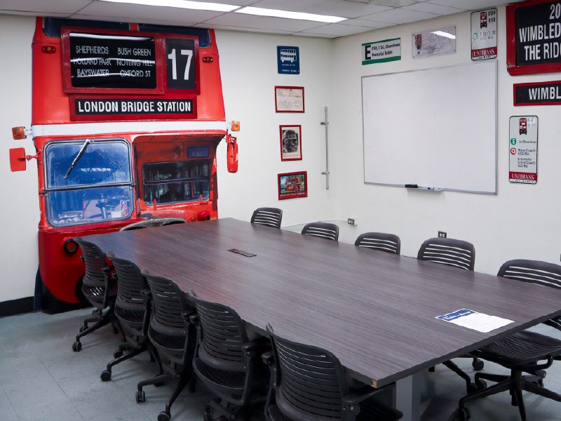 Conference table beside a wall built to resemble the front of a red Unitrans double-decker bus, with a whiteboard and framed transit memorabilia.